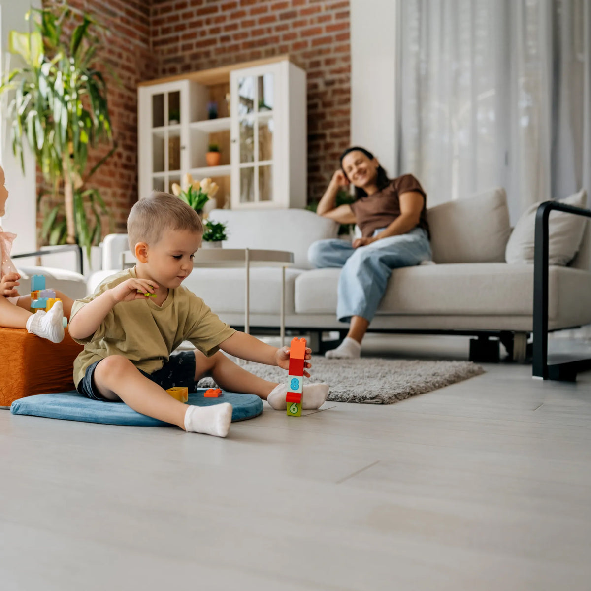 Kind spielt, Mama sitzt entspannt auf dem Sofa